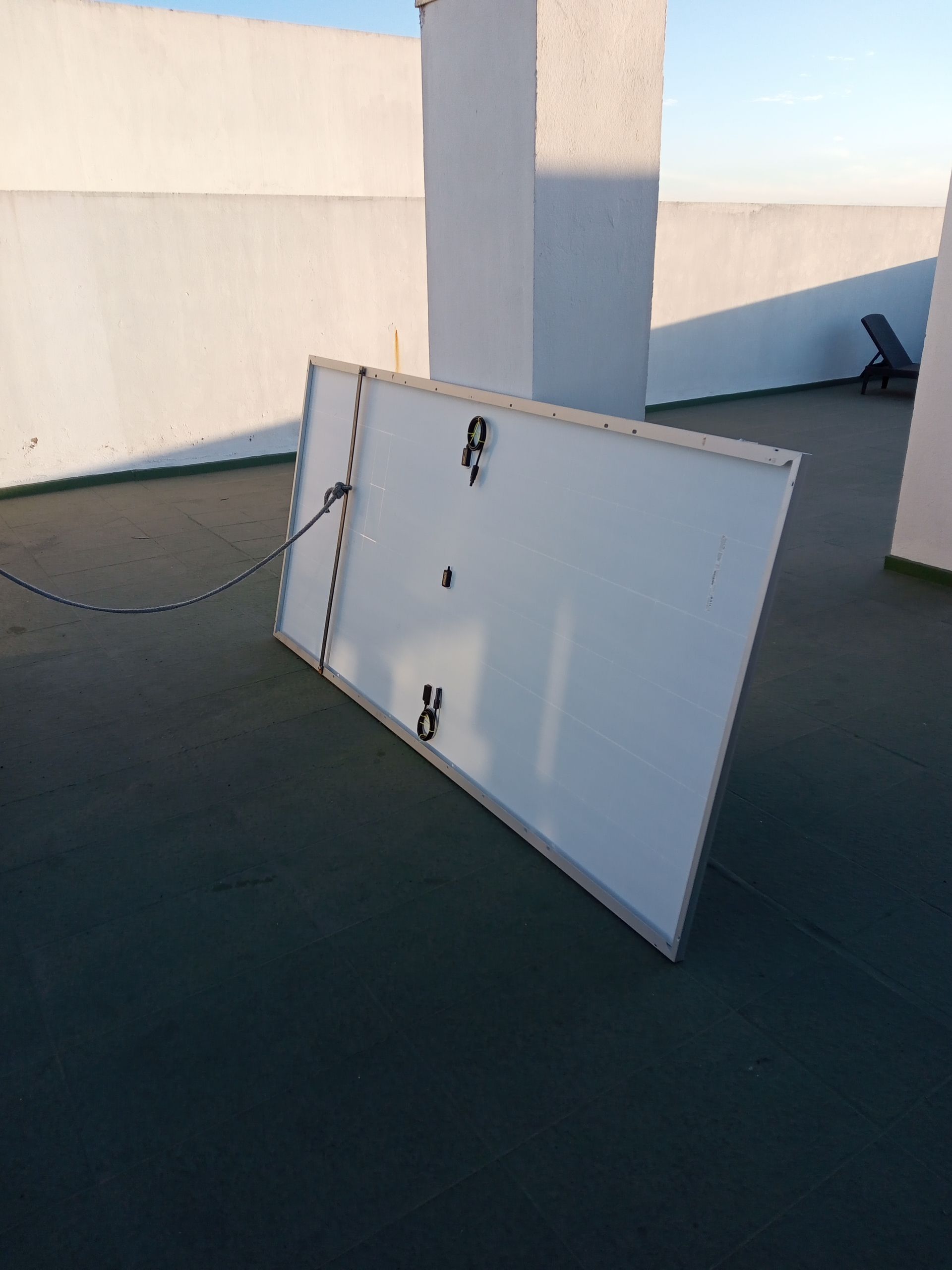 Un gran panel o puerta blanca apoyada contra una pared en una azotea, con un cable cerca.