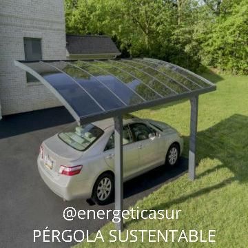 Coche blanco bajo una pérgola con paneles solares junto a una casa, con árboles al fondo.