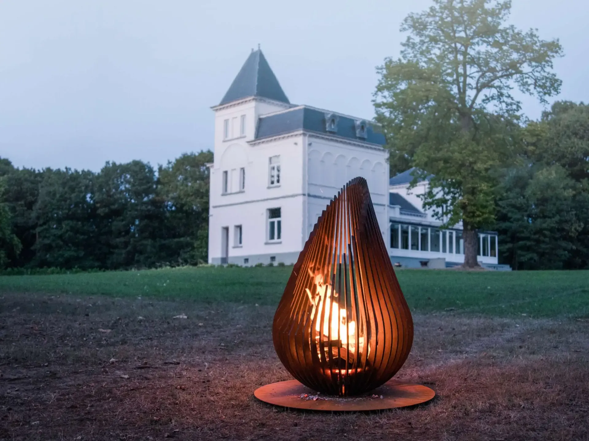 Beleuchtete Feuerskulptur auf einem Rasen vor einem weißen Haus in der Abenddämmerung