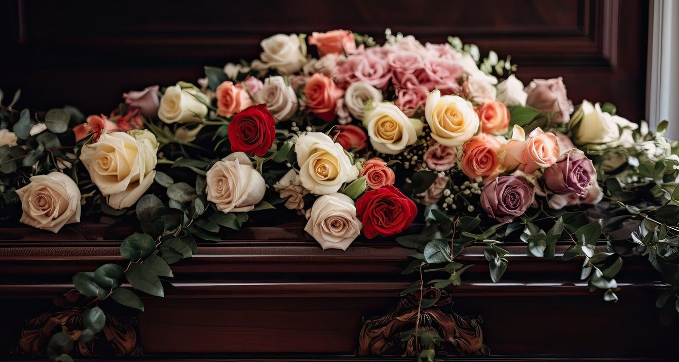 Assorted roses and greenery arranged in a floral spray on a dark wooden casket