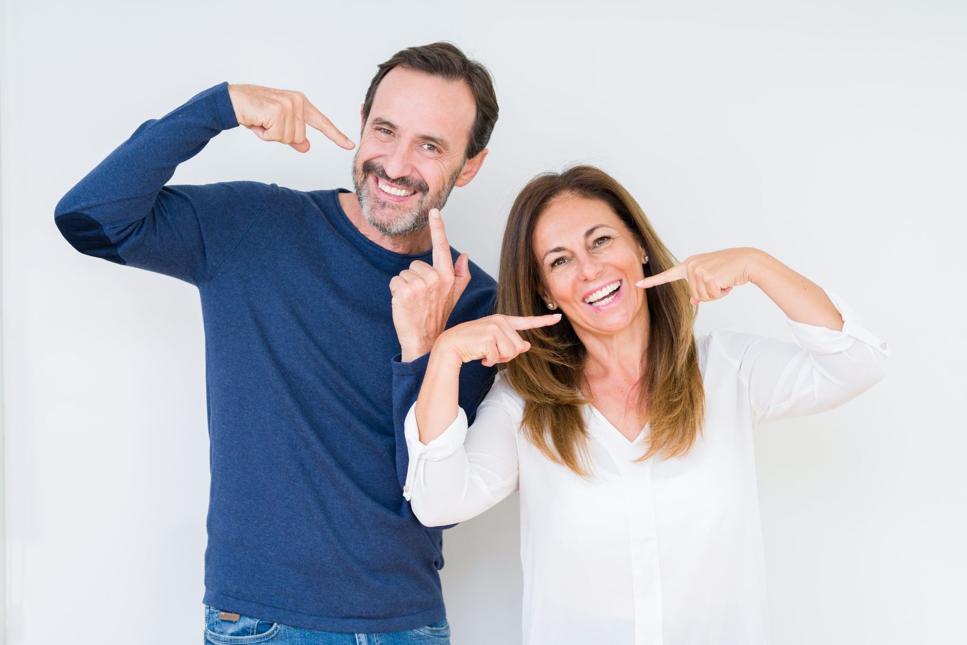 A man and a woman are smiling and pointing at their teeth.
