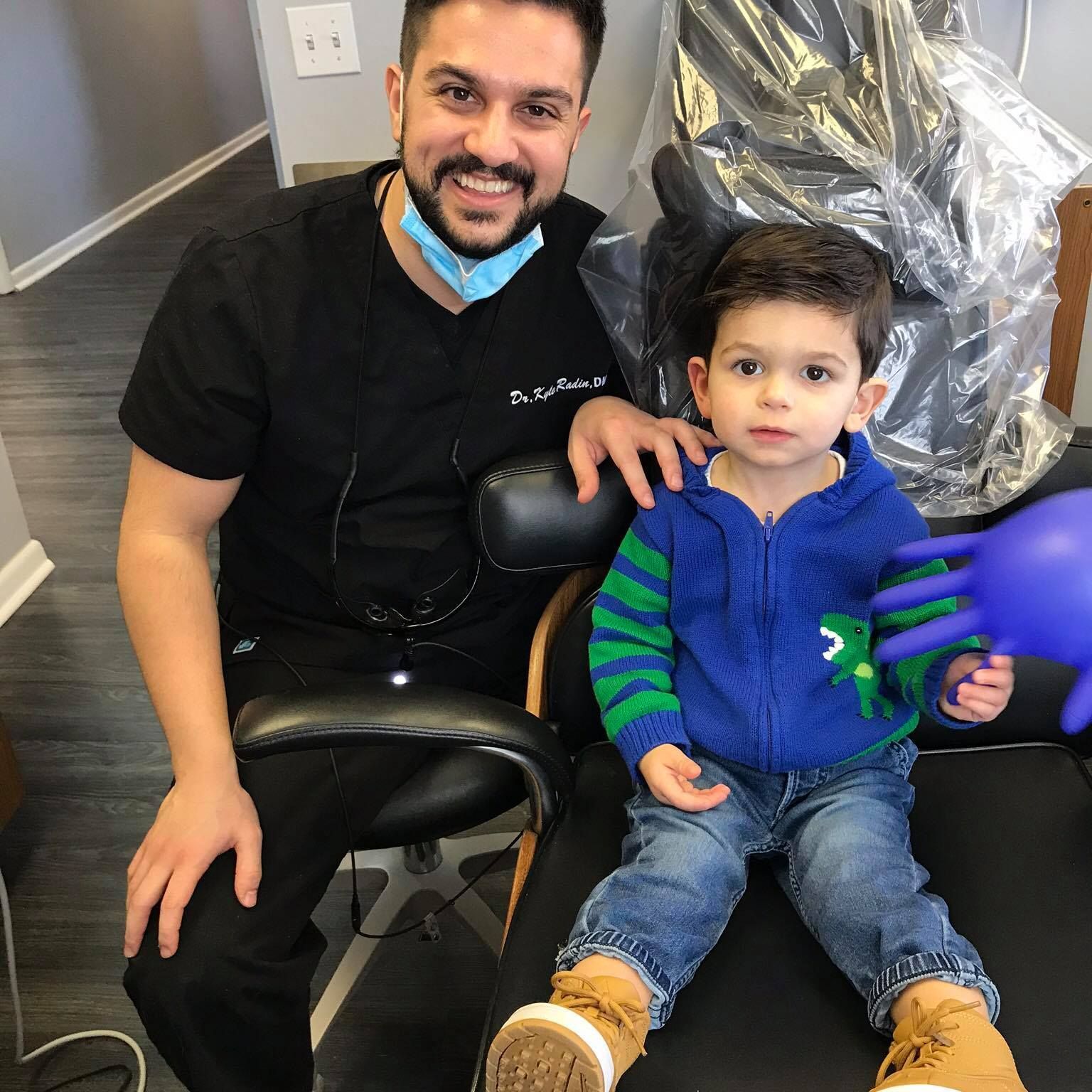 A dentist is sitting next to a little boy in a dental chair