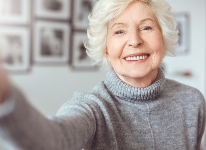 An elderly woman is taking a selfie and smiling.