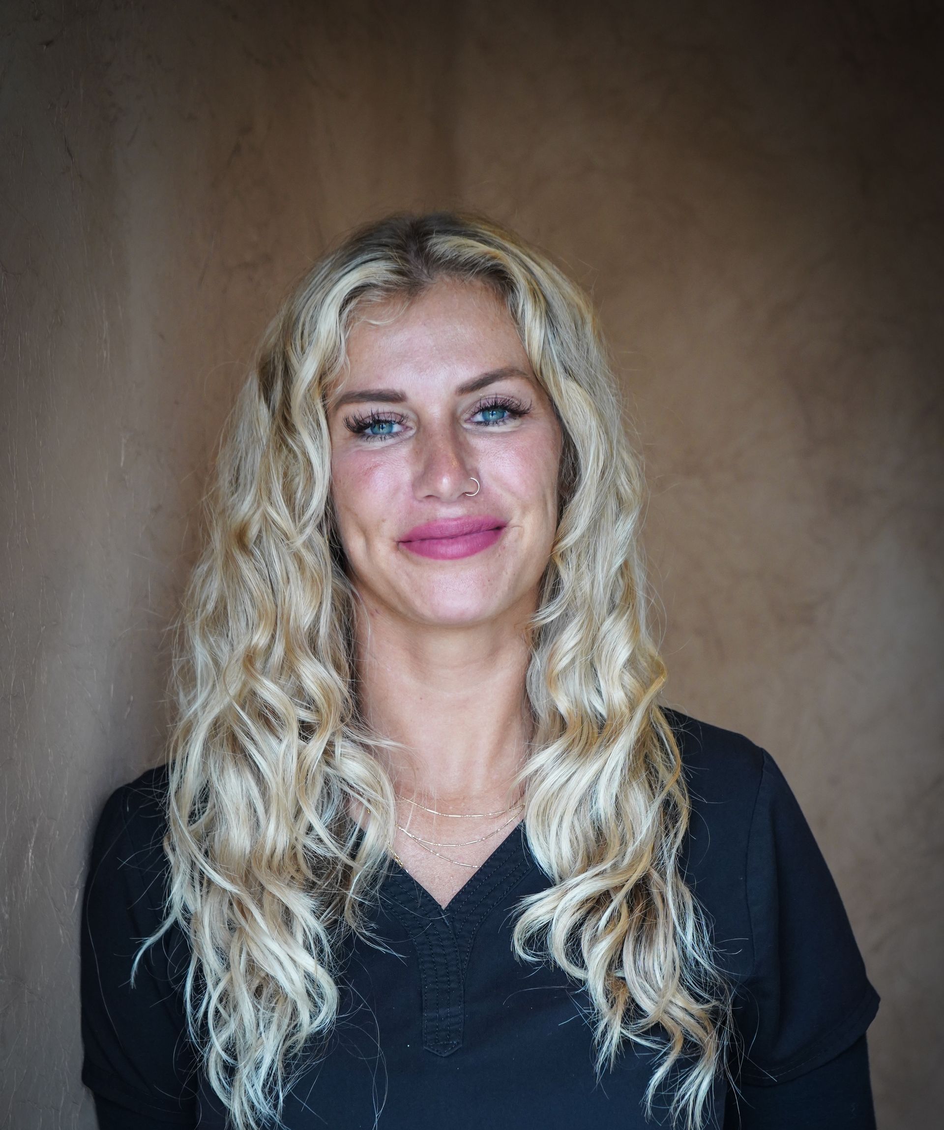 A woman with long blonde hair and blue eyes is wearing a black shirt.