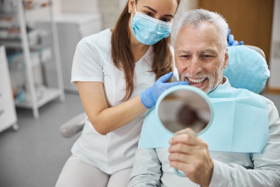 A dentist is looking at a patient 's teeth in a mirror.