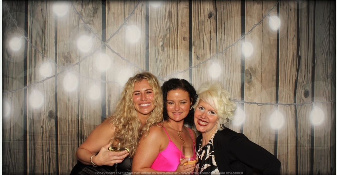 Three women are posing for a picture in front of a wooden wall.