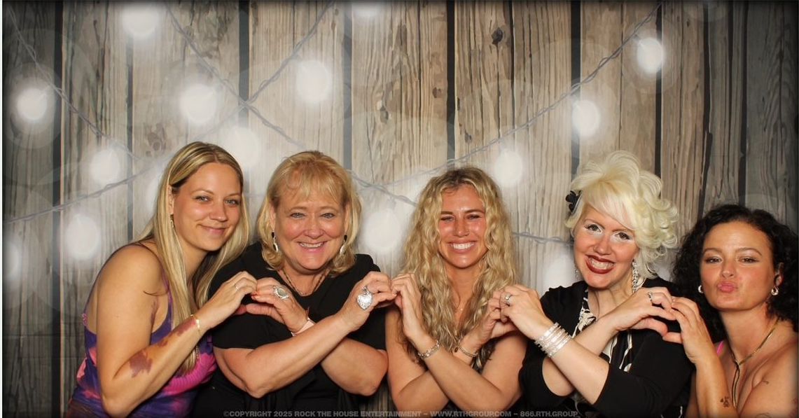 A group of women are posing for a picture in front of a wooden wall.