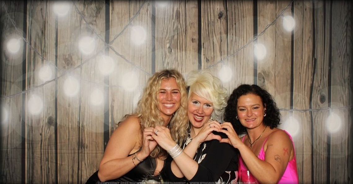 Three women are posing for a picture in front of a wooden wall.
