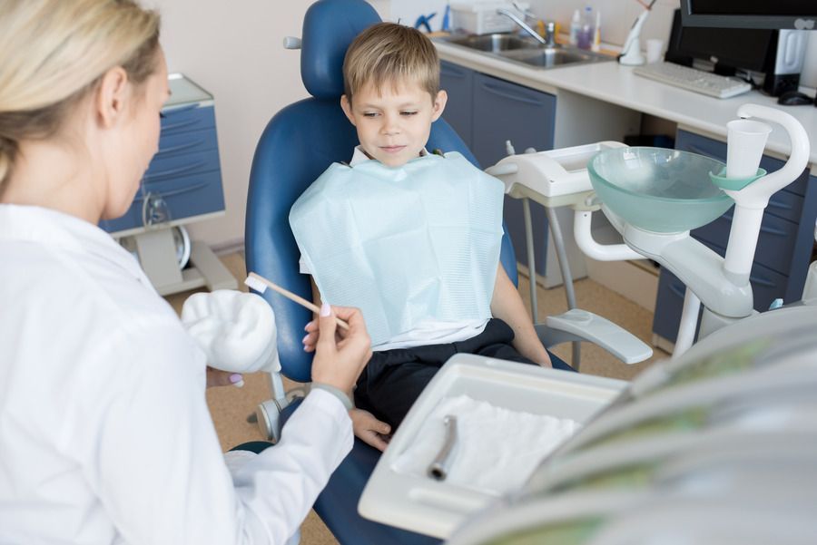 A young boy is sitting in a dental chair while a dentist brushes his teeth.