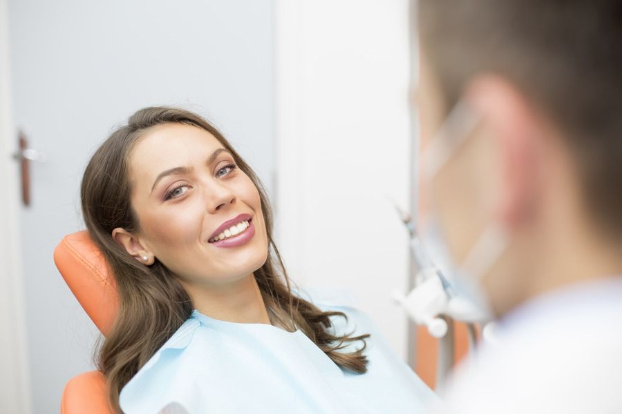 A woman is sitting in a dental chair smiling at the dentist.