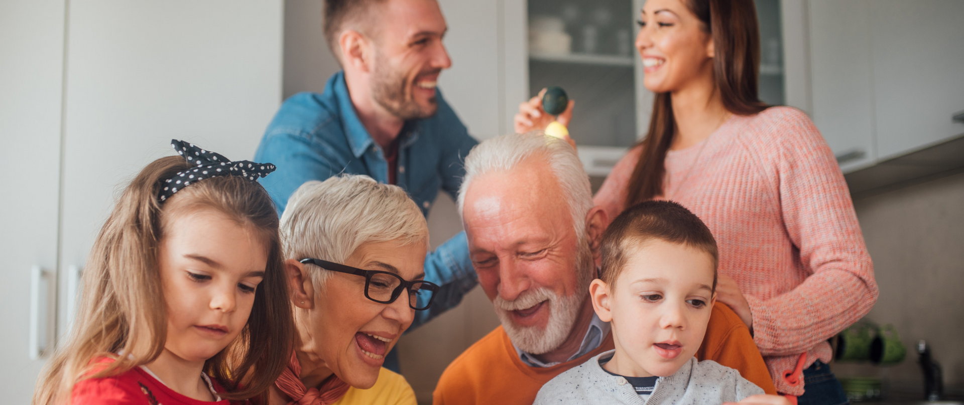 A family is sitting in a kitchen looking at a tablet.