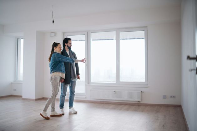 Couple in empty room, looking at window, woman gesturing.