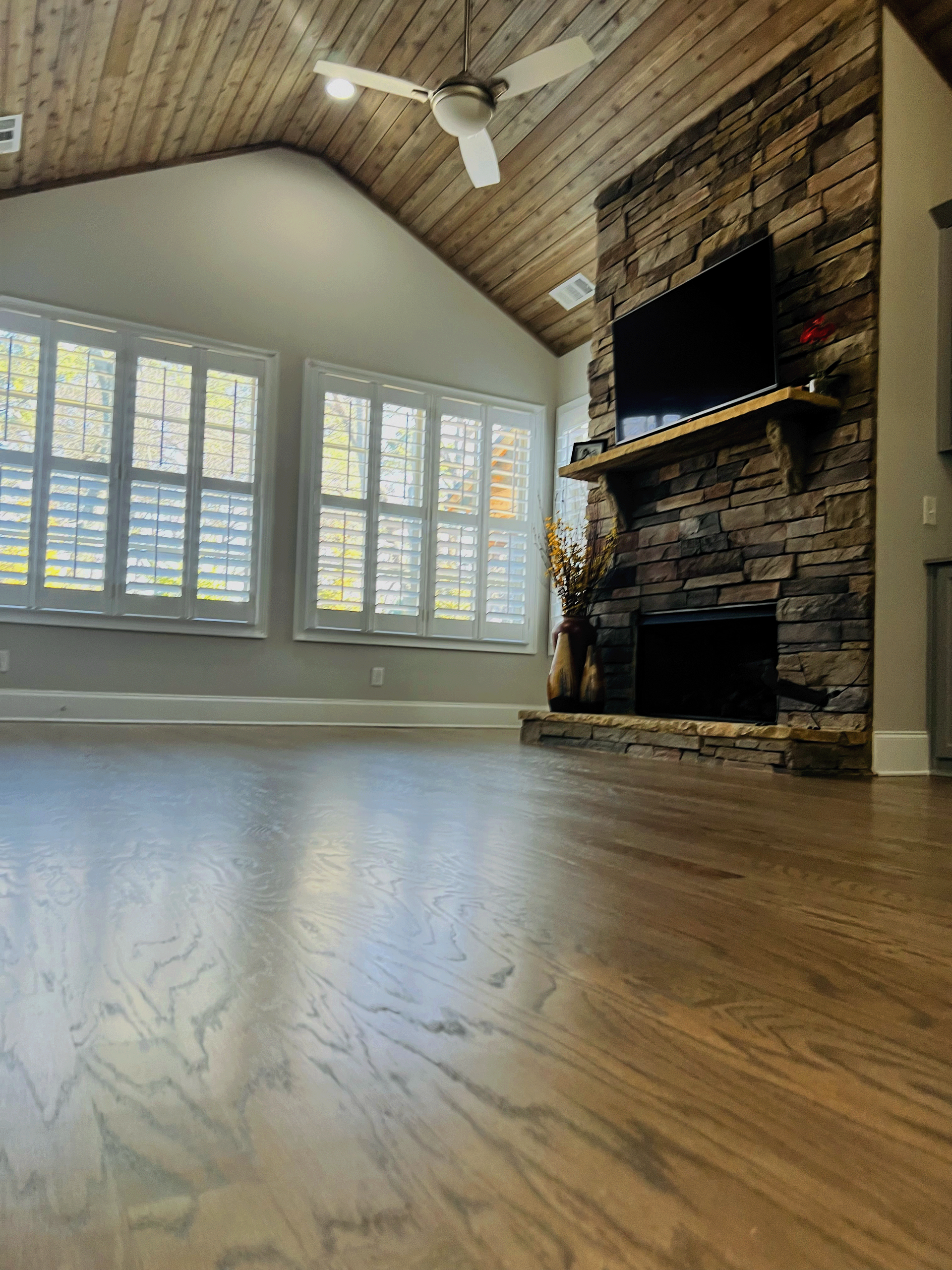 A living room with hardwood floors , a stone fireplace and a flat screen tv.