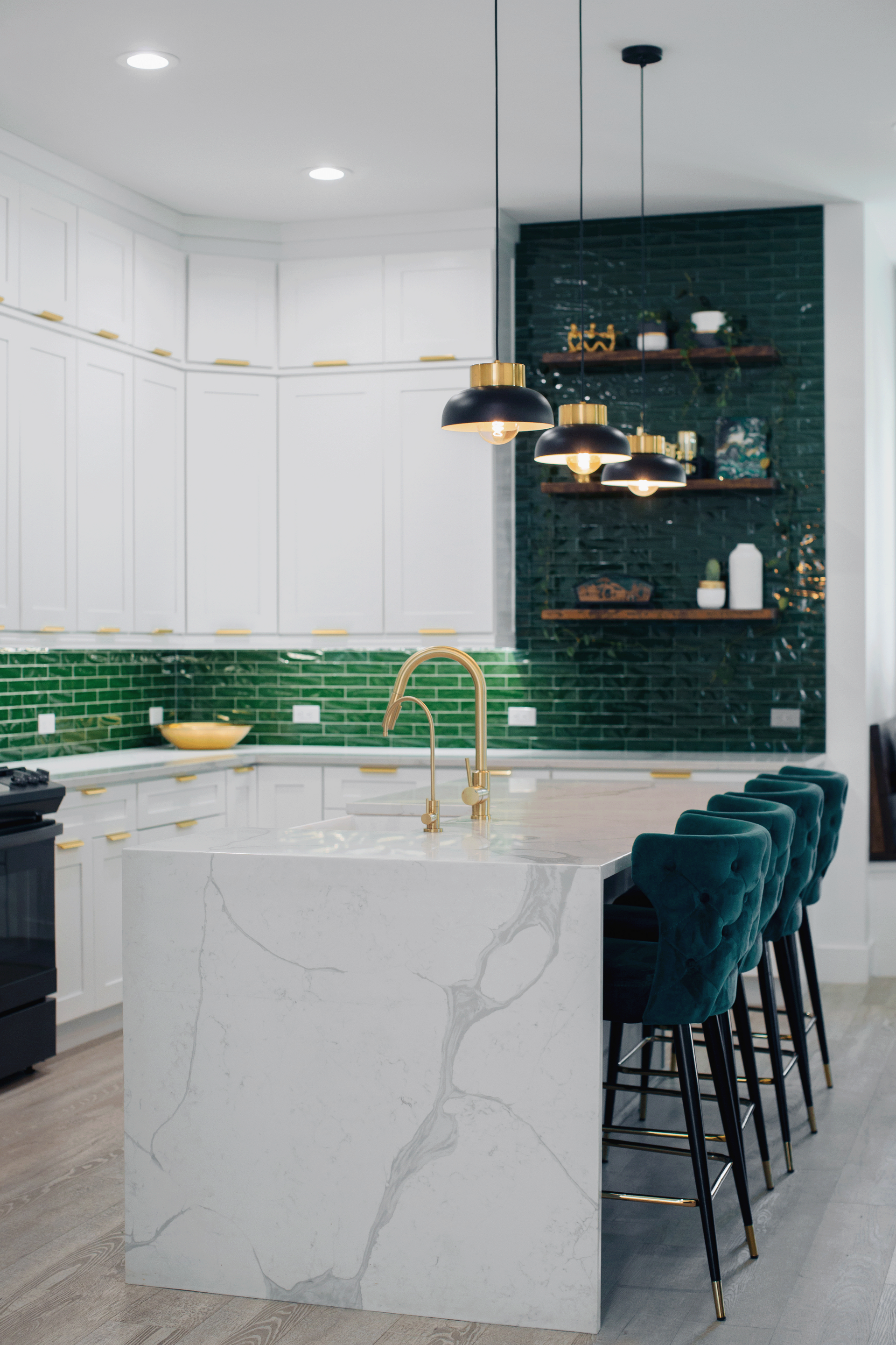 A kitchen with green tiles , white cabinets , a large island , and a row of bar stools.