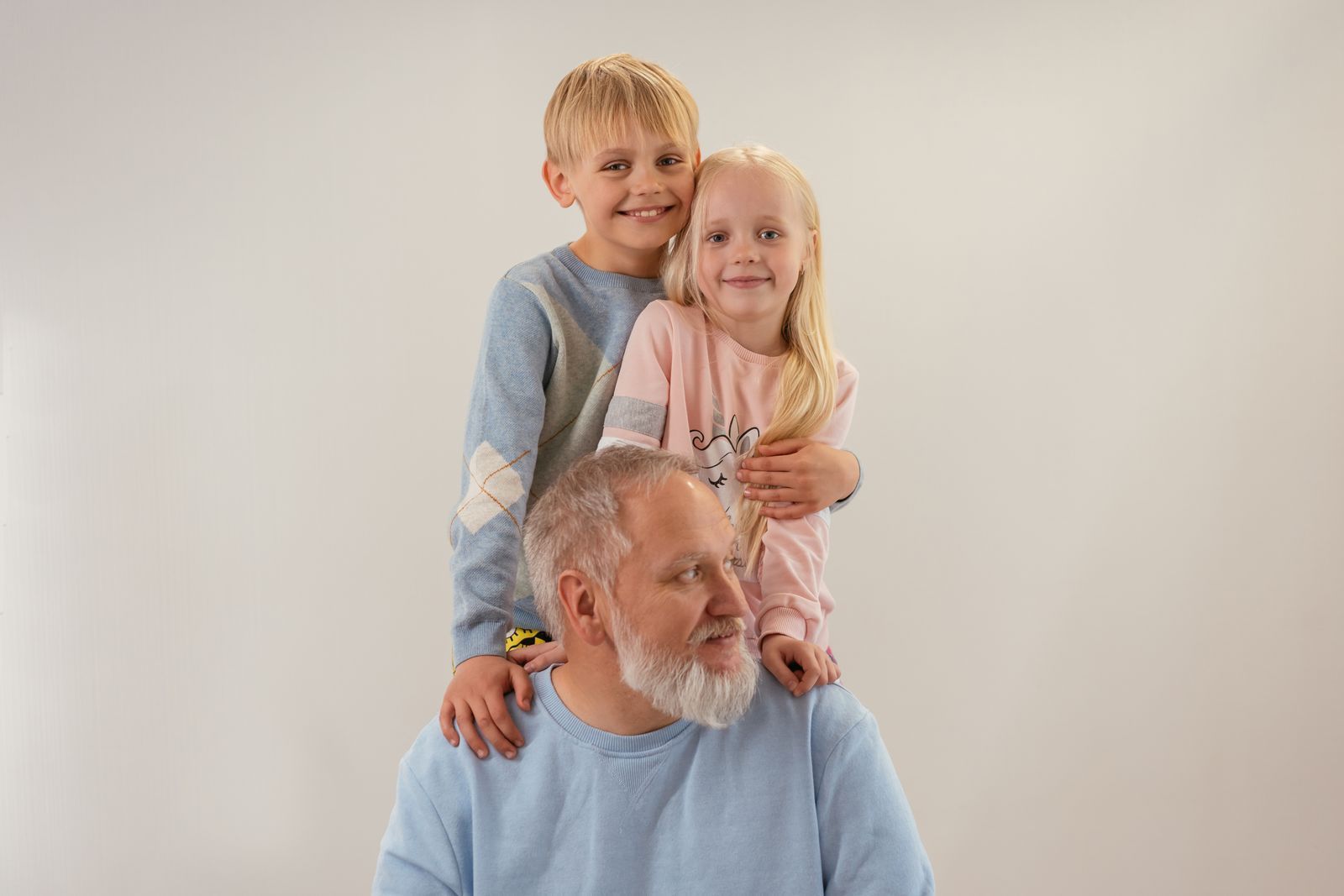 Two children smiling and embracing an older man against a plain white background
