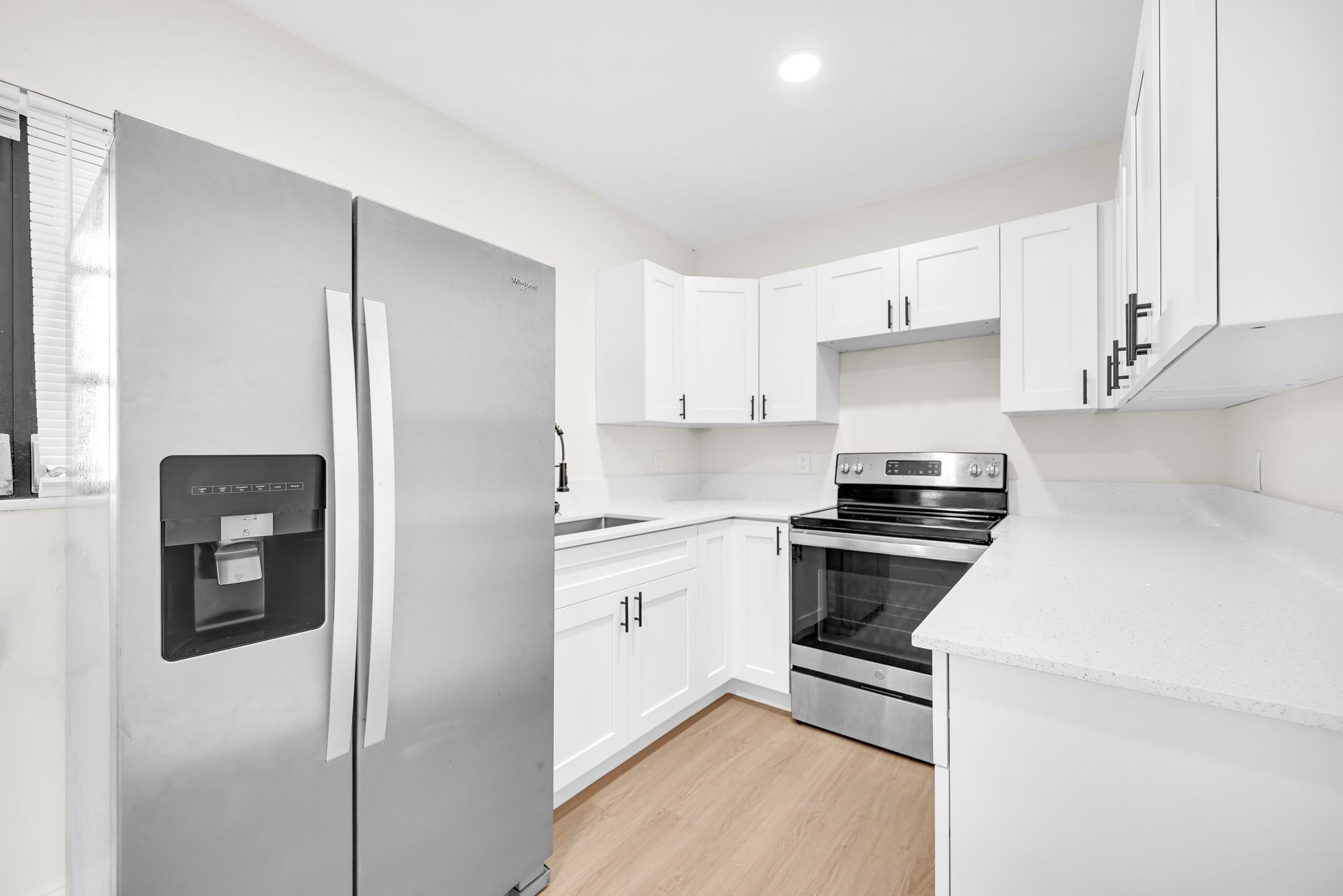 Bright white kitchen with stainless steel refrigerator, oven, and cabinets, plus light wood flooring