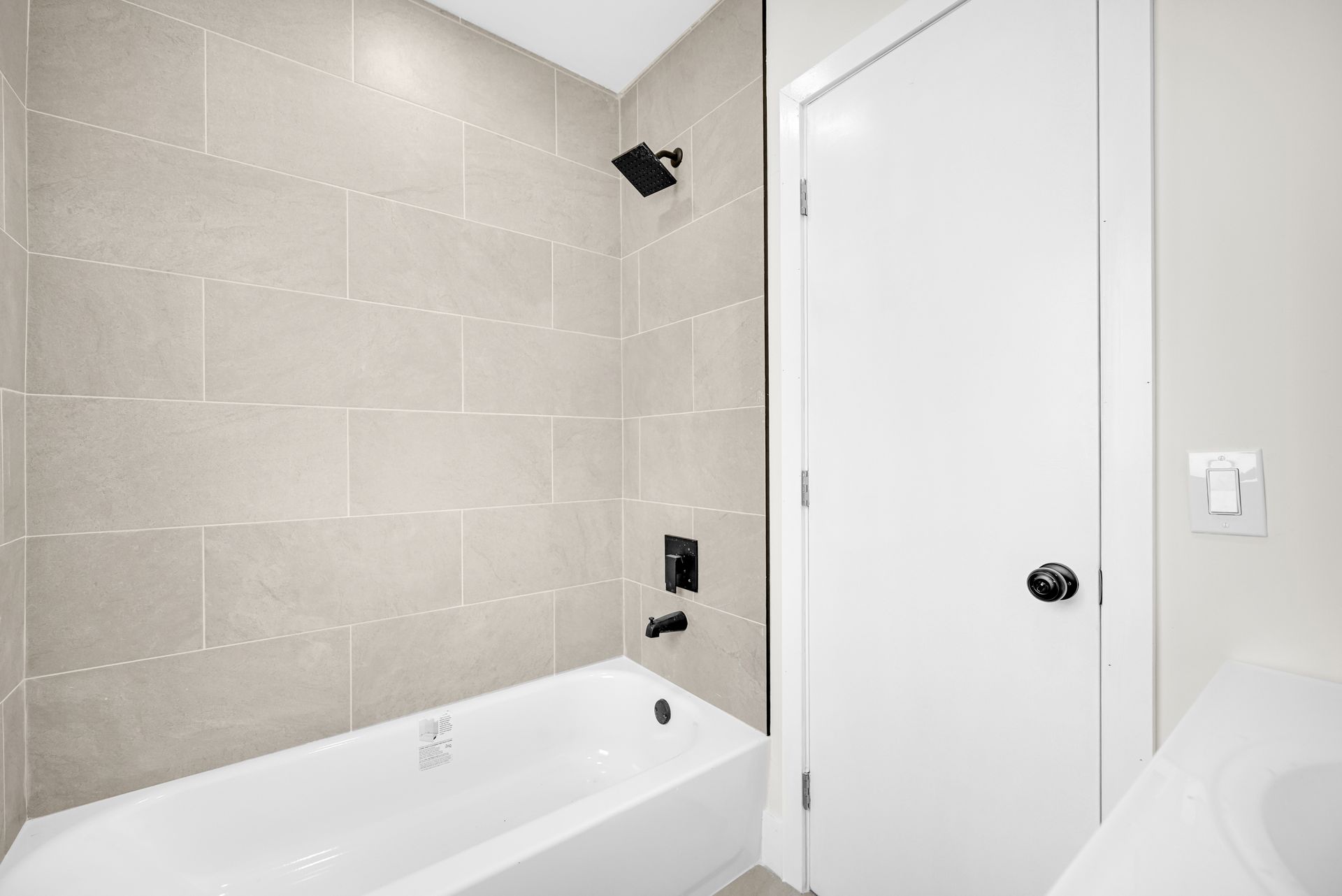 Bright bathroom with tiled walls, white bathtub, and closed white door
