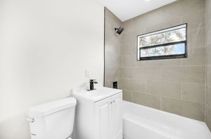 Modern bathroom with white toilet, sink vanity, and tiled bathtub shower with small window