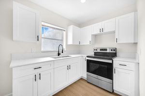 Bright white kitchen with stainless steel stove, corner sink, and light wood flooring