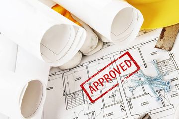 Blueprints with a red “APPROVED” stamp and rolled architectural plans