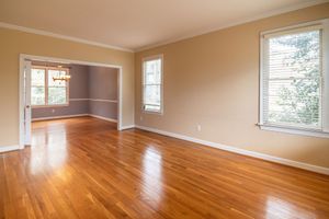 Empty living room with polished hardwood floors, beige walls, and large windows letting in daylight