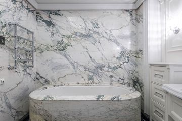 Marble bathroom with built-in tub, gray-veined walls, and white cabinetry