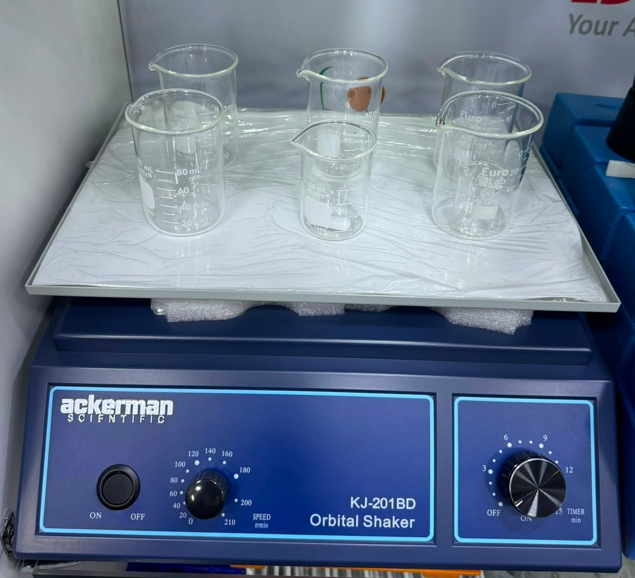 Agitador orbital de laboratorio con varios vasos de precipitados de vidrio sobre una plataforma blanca.