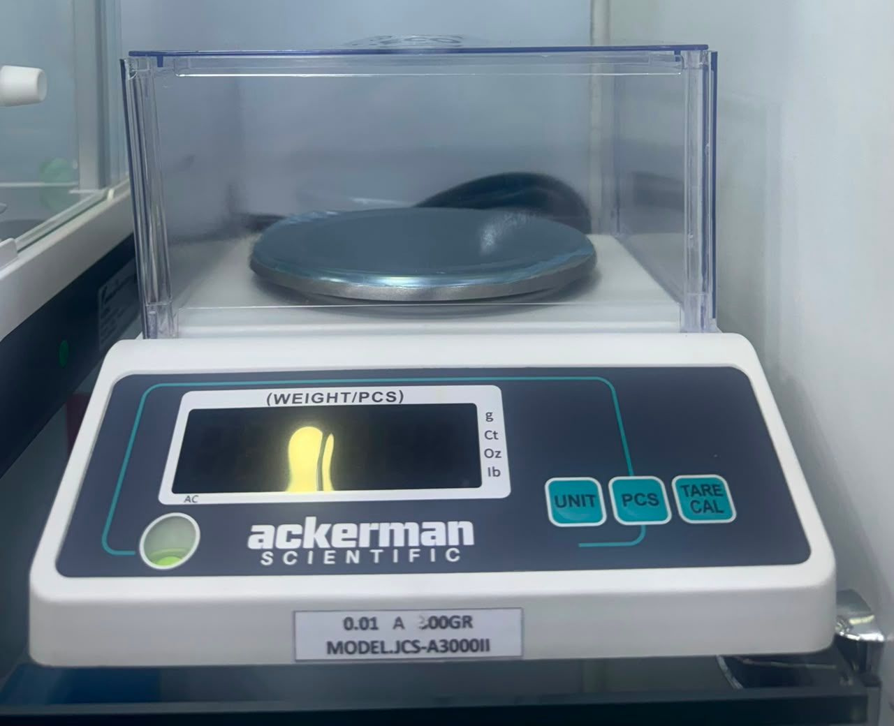 Balanza de laboratorio digital con tapa y pantalla transparentes, de la marca Ackerman, sobre una encimera.