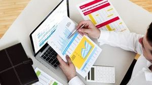 Person examining financial documents at a desk with a laptop and calculator.