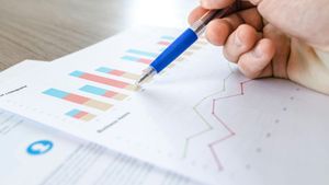 Hand holding blue pen pointing at a bar graph and line graph on a white paper.
