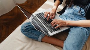 Person typing on a laptop, sitting with crossed legs, wearing blue jeans.