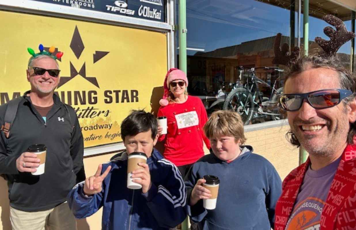 Group of people outside a business, holding coffee cups, some wearing holiday accessories.