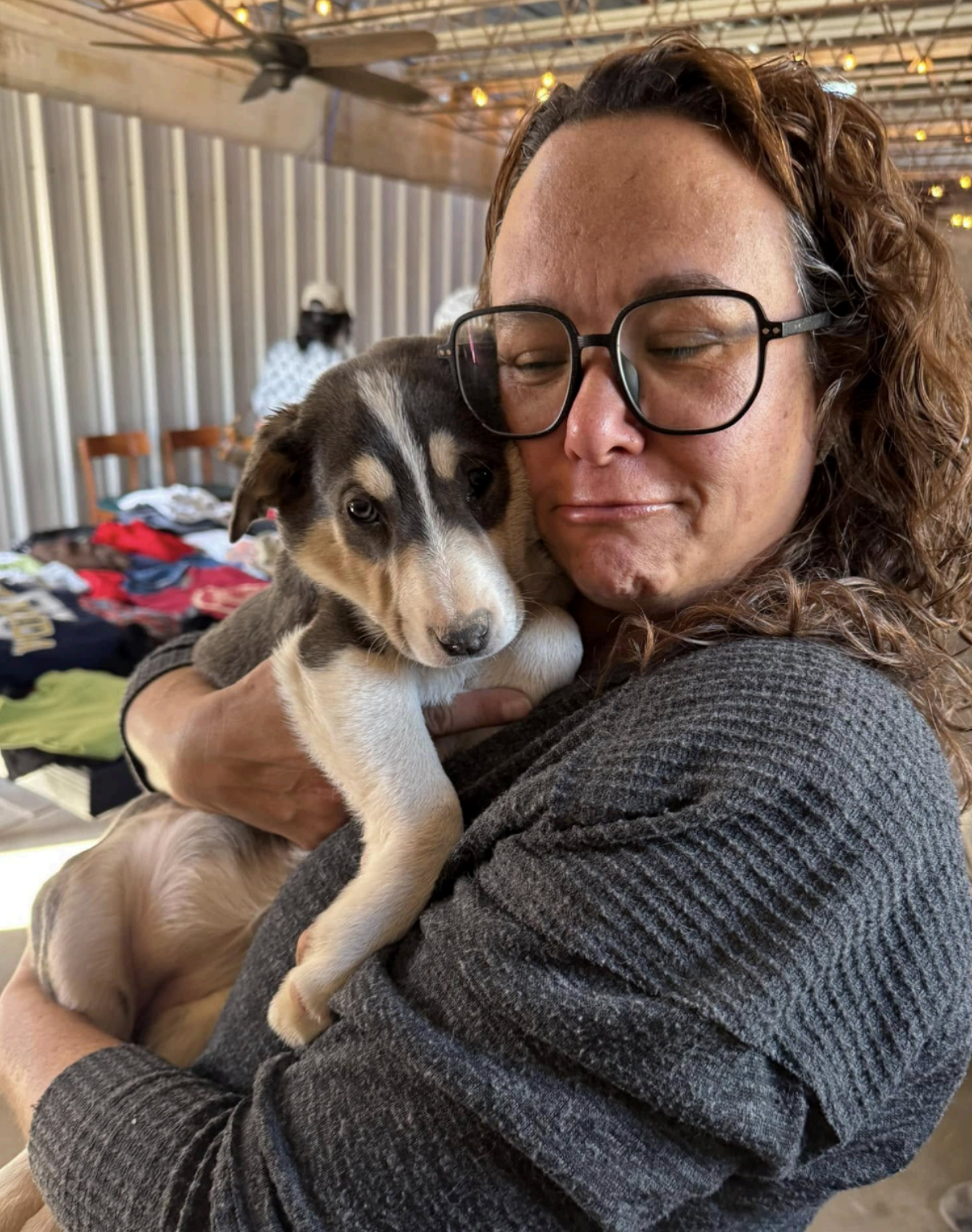 Woman holding a small puppy with black and white markings; both are indoors, under a covered area.