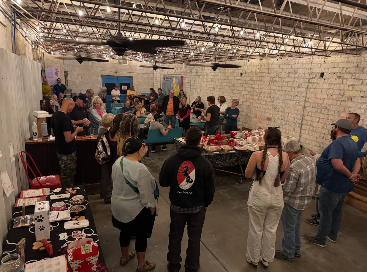 People browse vendor tables at an indoor market with brick walls, under string lights.
