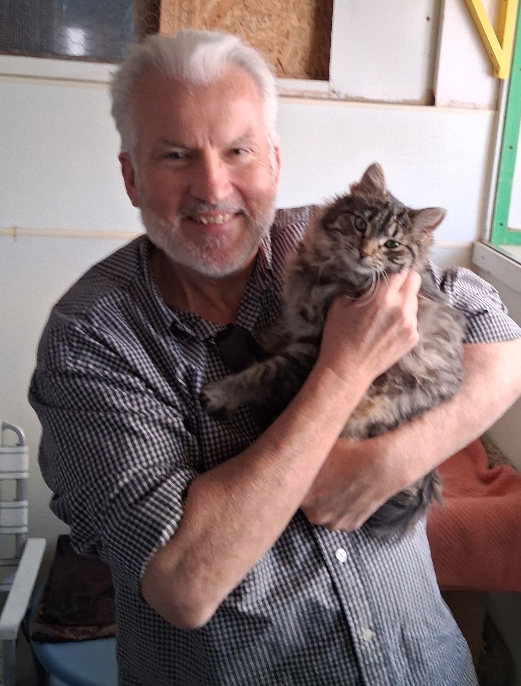 Smiling man holding a fluffy tabby cat indoors