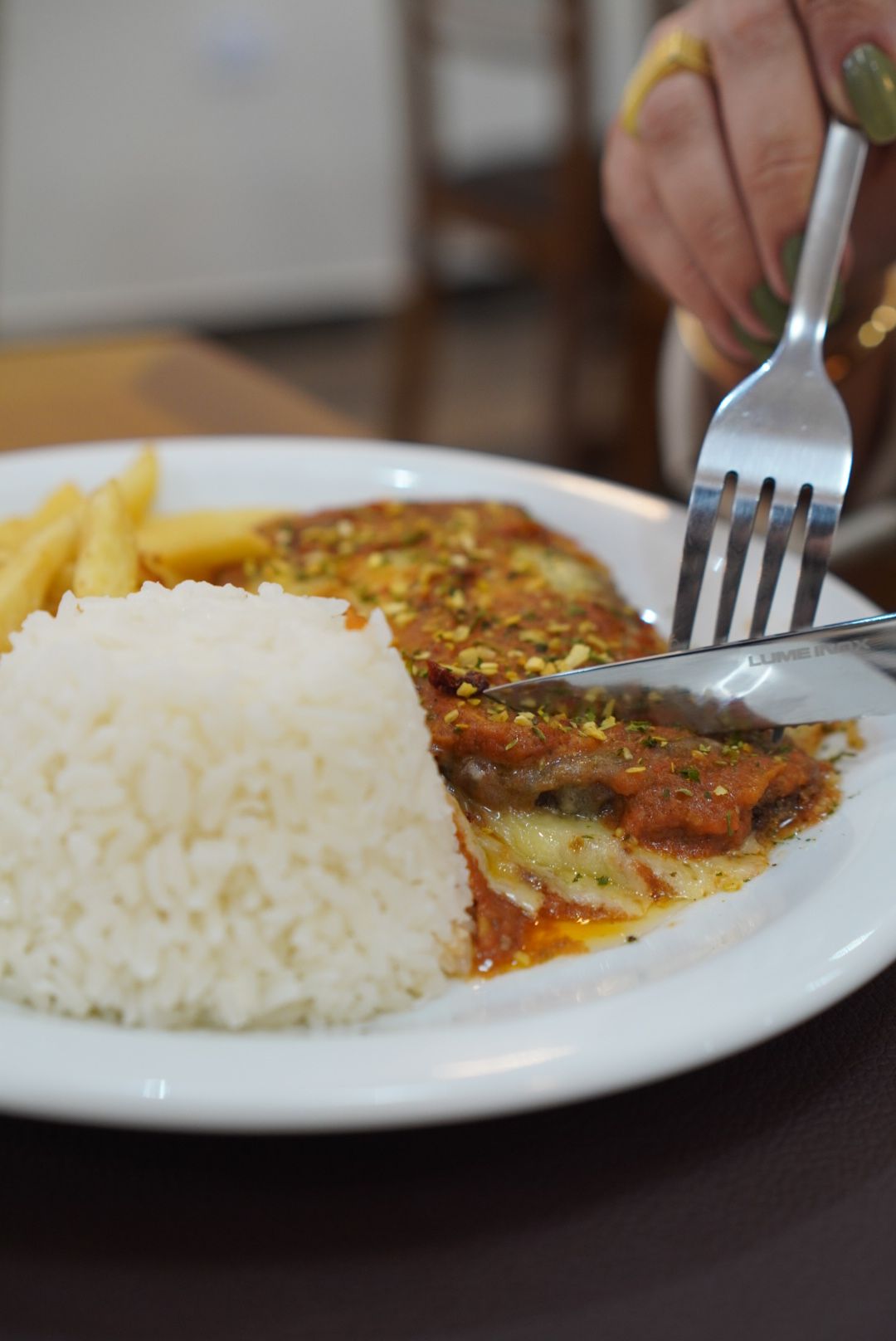 Uma pessoa está cortando um pedaço de carne em um prato com arroz e batatas fritas.
