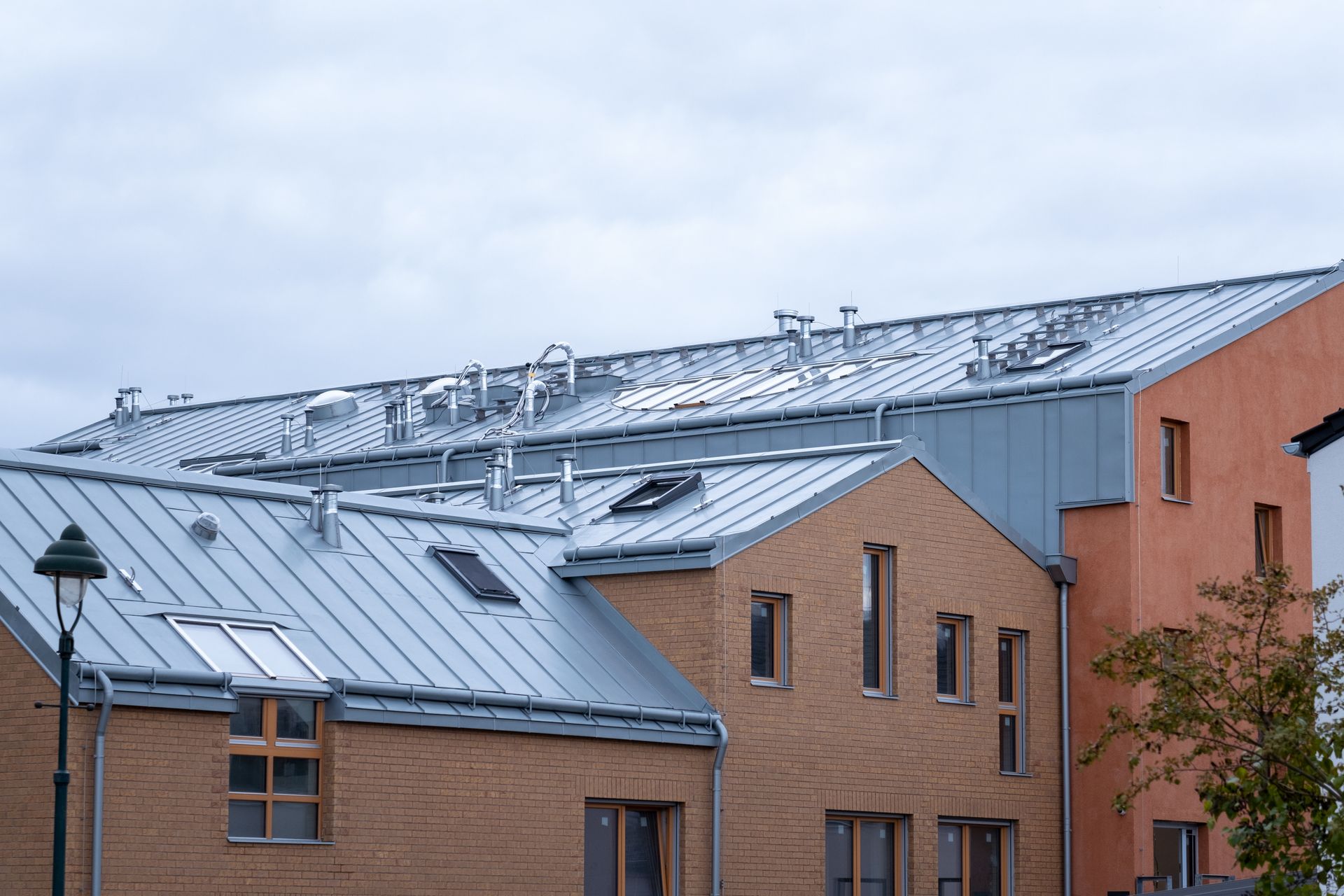 Buildings with metal roofs and various chimneys against a cloudy sky. Buildings with metal roofs and various chimneys against a cloudy sky.