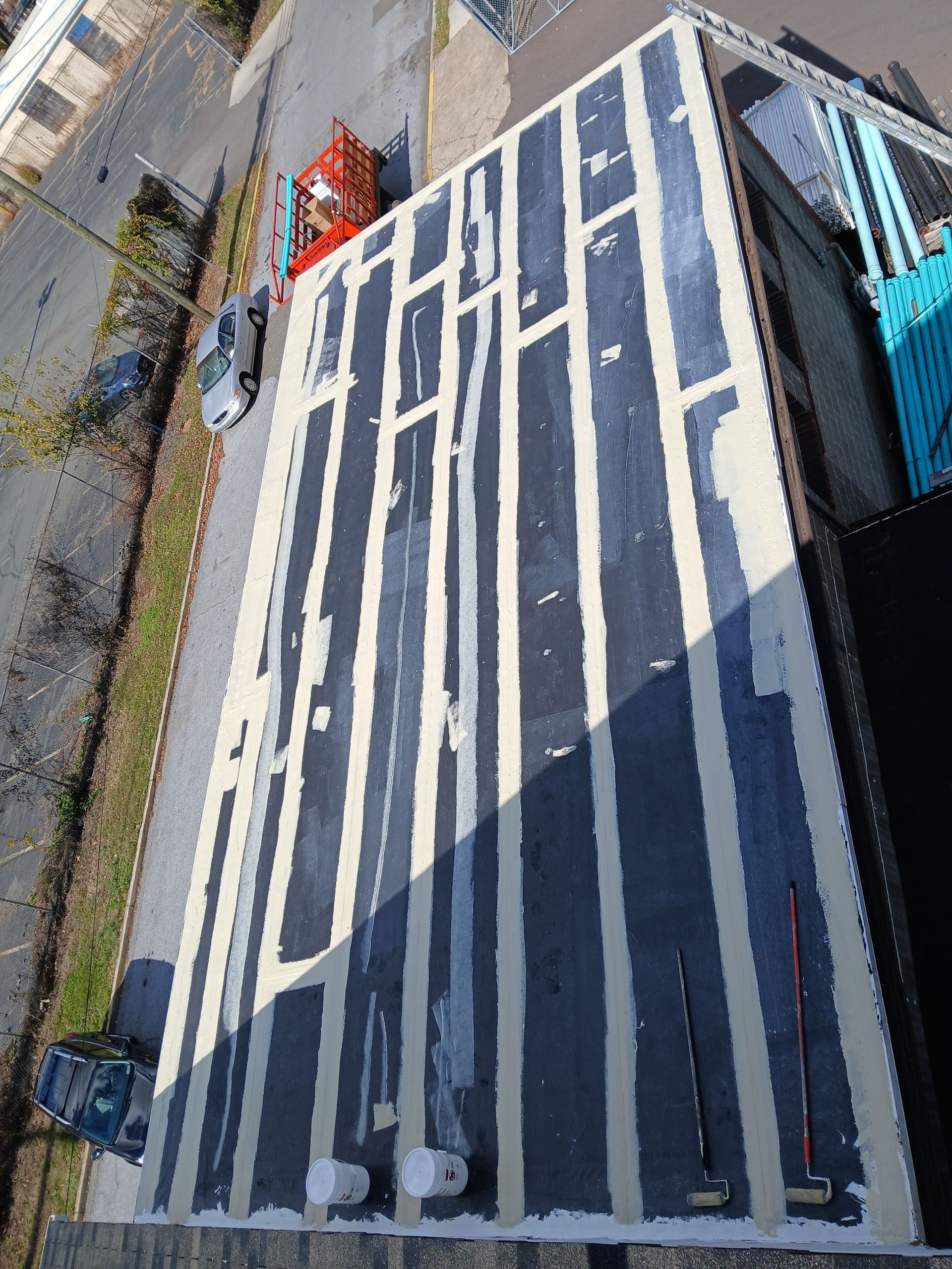 Aerial view of a striped rooftop beside a road, with orange construction equipment and parked vehicles below