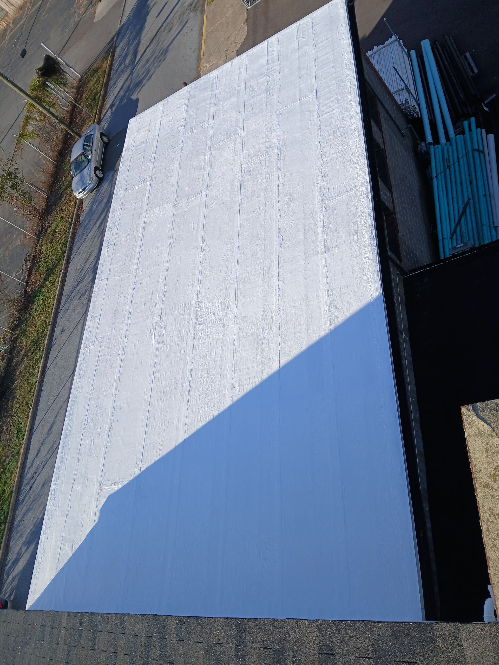 Aerial view of a white roof with a blue triangular section beside stacked blue materials and pavement.