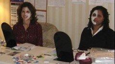 Two people sitting at a table with black chairs and papers in a room