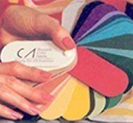 Hands holding a round compact next to a fan of colorful nail polish swatches.