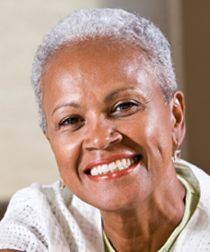 Smiling person with short gray hair in a white sweater against a neutral background