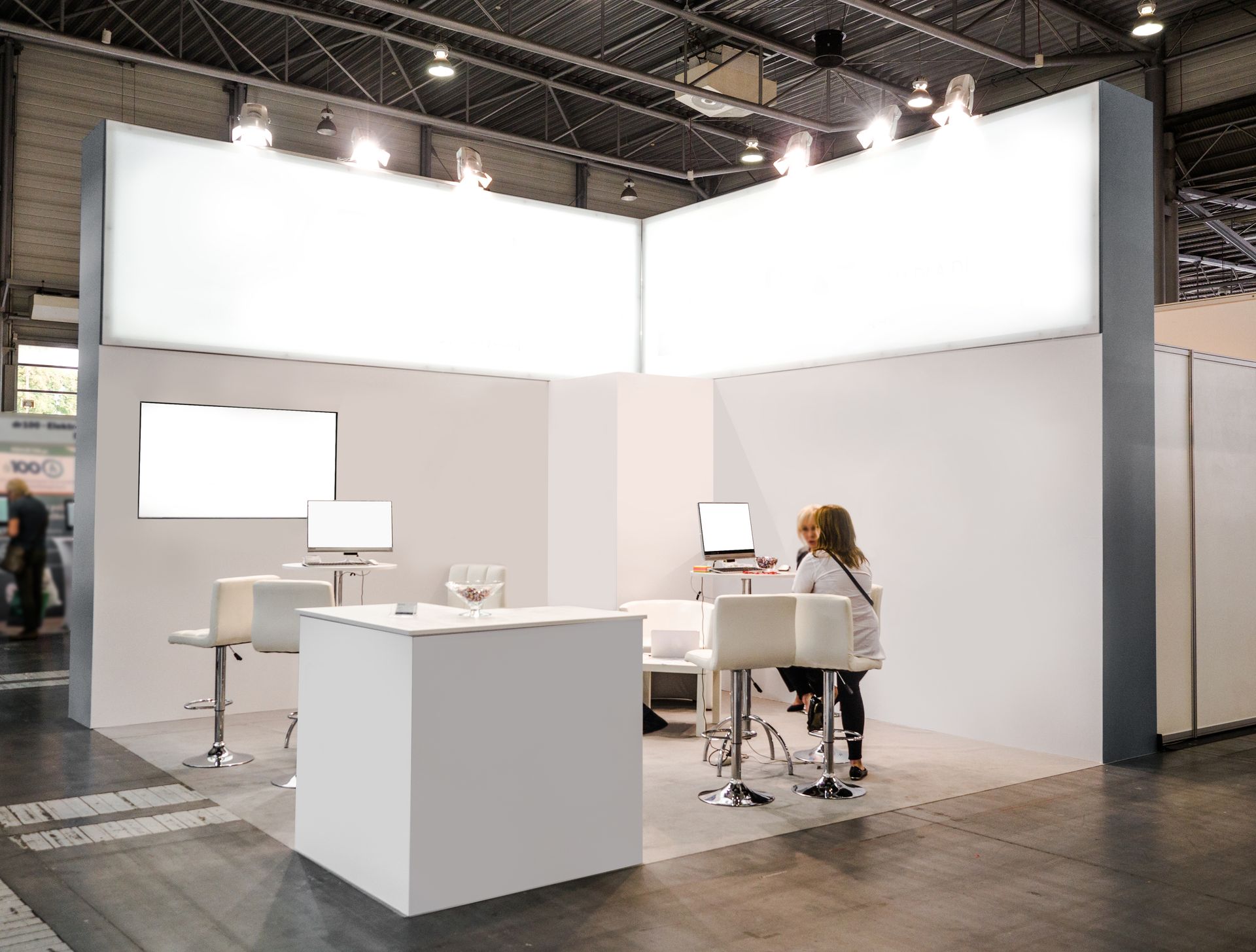 An exhibition stand, featuring a futuristic interior, suspended lighting fixtures, and a screen. An exhibition stand, featuring a futuristic interior, suspended lighting fixtures, and a screen.
