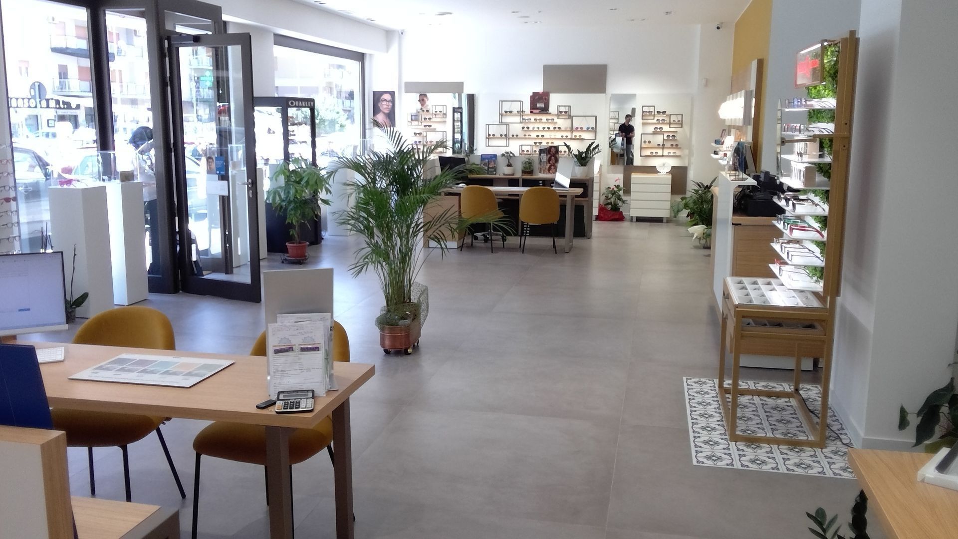 Luminoso interno di una caffetteria moderna con tavoli, sedie, scaffali e un ingresso in vetro.