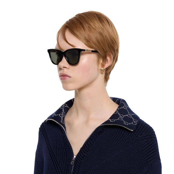 Donna con occhiali da sole rotondi a specchio, che tiene sulle tempie, con i capelli mossi dal vento.