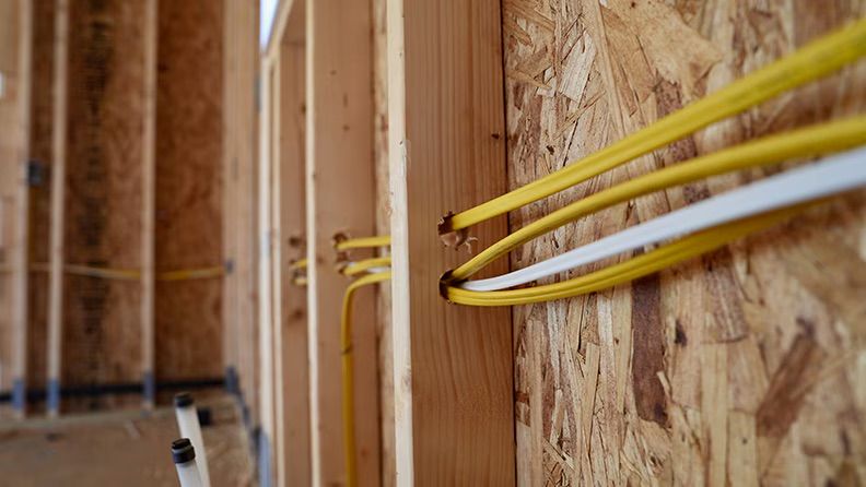 Electrical wiring running through holes in wooden wall studs in a room under construction.