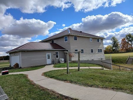 Suburban house with attached garage, curved driveway, and fenced yard under a cloudy blue sky