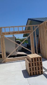 Framed wooden wall under construction beside a house, with a stack of cinder blocks in the foreground.