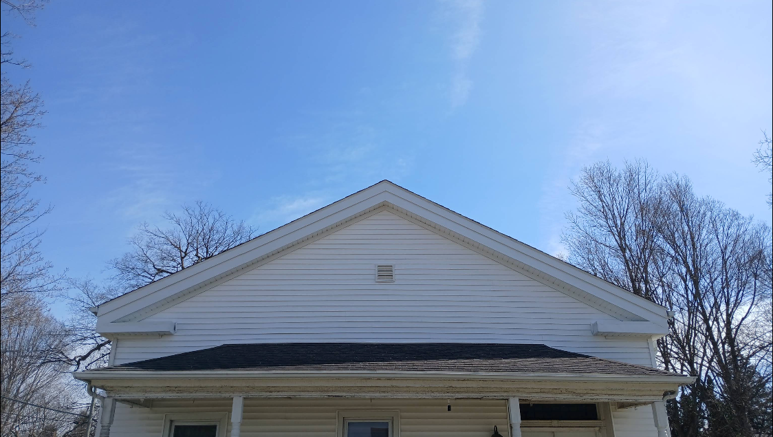 White house front with triangular gable and porch under a blue sky