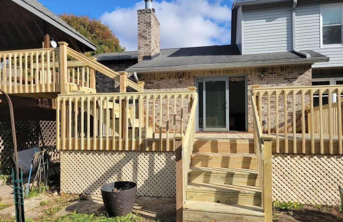 Backyard deck with wooden stairs, railing, lattice skirting, and a stone fireplace against a house.